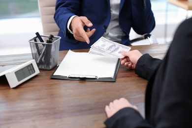 Photo of Woman giving bribe money to man at table, closeup