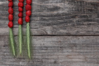 Grass stems with wild strawberries on wooden table, flat lay. Space for text
