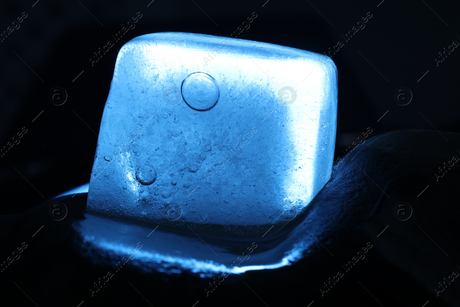 Photo of Crystal clear ice cube on dark background, closeup. Color tone effect