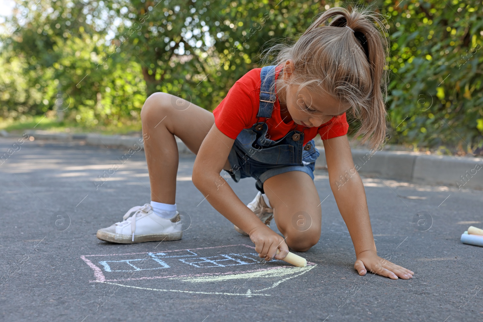 Photo of Cute little child drawing house with colorful chalk on asphalt