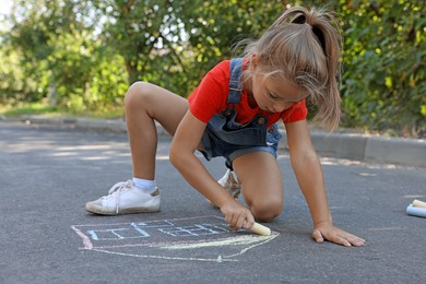 Cute little child drawing house with colorful chalk on asphalt