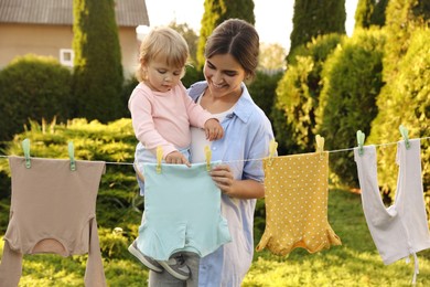 Photo of Mother and daughter hanging clothes with clothespins on washing line for drying in backyard