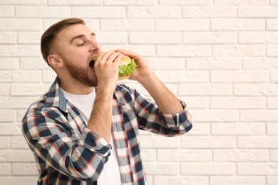 Photo of Young man eating tasty burger near brick wall. Space for text