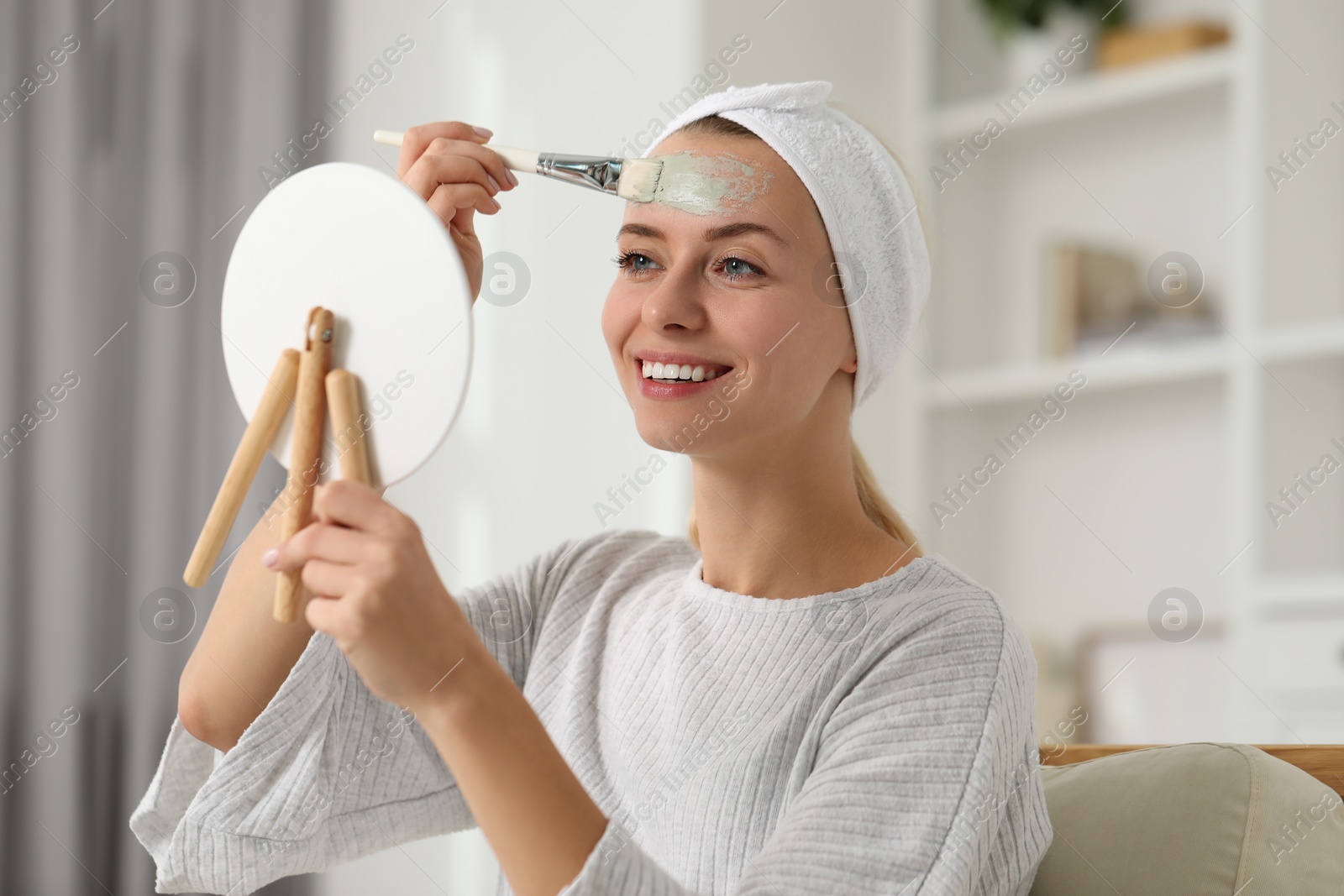 Photo of Young woman applying face mask in front of mirror at home. Spa treatments