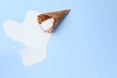 Melted ice cream and wafer cone on light blue background, top view. Space for text