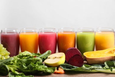 Glasses with different juices and fresh ingredients on light background