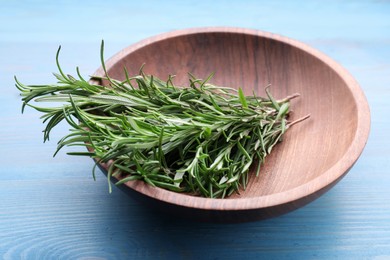 Photo of Sprigs of fresh rosemary in bowl on light blue wooden table, closeup