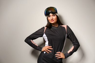Photo of Woman wearing thermal underwear and goggles on light grey background. Winter sport clothes