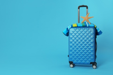 Stylish suitcase with towel and sea star on color background. Space for text