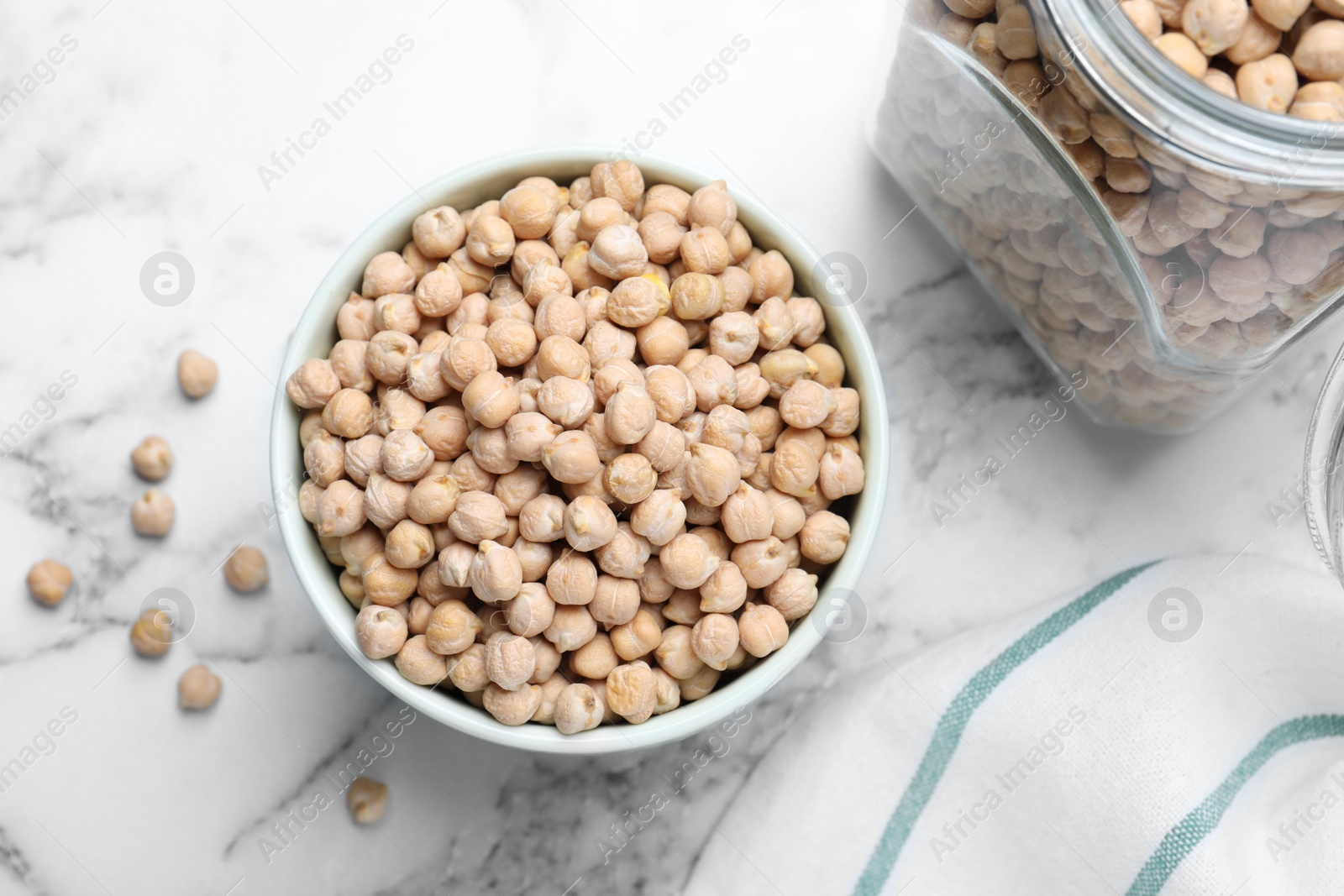 Photo of Bowl and jar with chickpeas on white marble table, flat lay