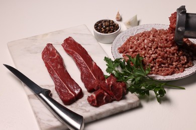 Photo of Manual meat grinder with beef, peppercorns and parsley on white table