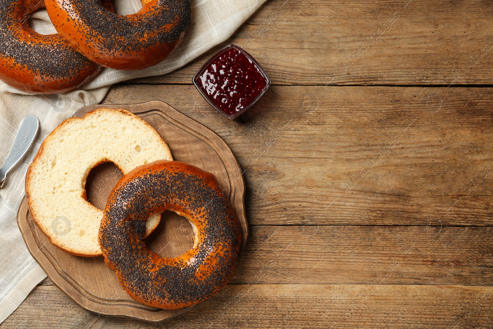 Photo of Delicious fresh bagels with poppy seeds and jam on wooden table, flat lay. Space for text