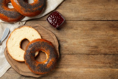 Delicious fresh bagels with poppy seeds and jam on wooden table, flat lay. Space for text