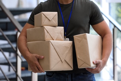Photo of Young courier with parcels indoors, closeup. Delivery service