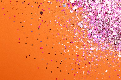 Photo of Shiny bright pink glitter on orange background, flat lay