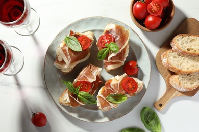 Tasty sandwiches with cured ham, basil and tomatoes on white marble table, flat lay