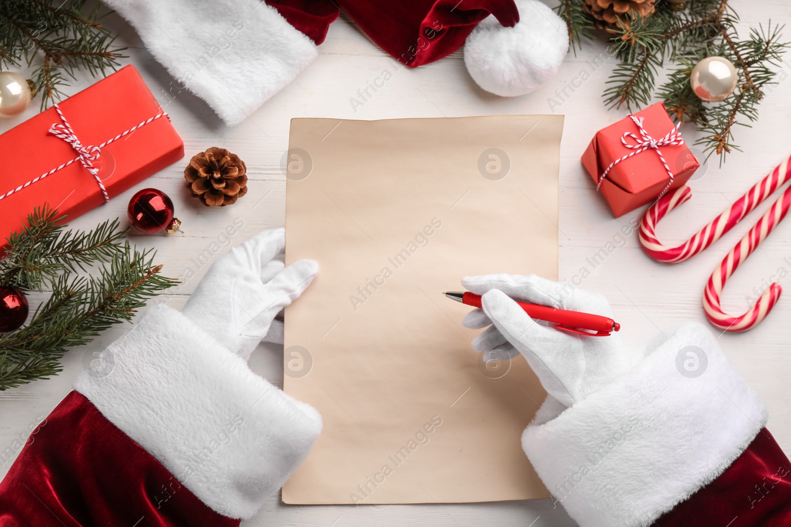 Photo of Santa Claus writing letter at white wooden table, top view. Christmas celebration