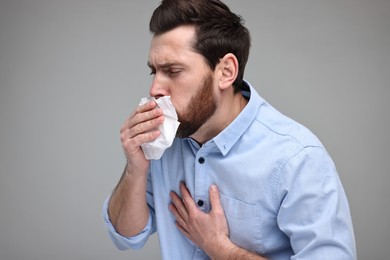 Photo of Sick man with tissue coughing on light grey background