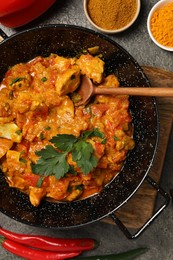 Delicious chicken curry and spices on grey table, flat lay