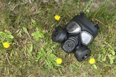 One gas mask on green grass outdoors, top view. Space for text