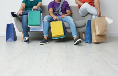 Photo of Group of young men with shopping bags sitting on sofa near light wall