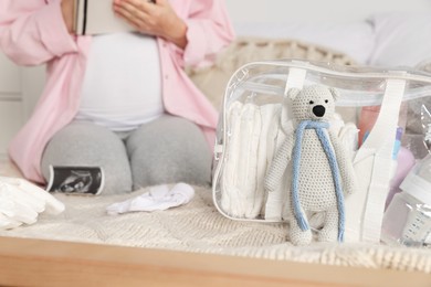 Photo of Pregnant woman preparing list of necessary items to bring into maternity hospital in bedroom, focus on bag and toy