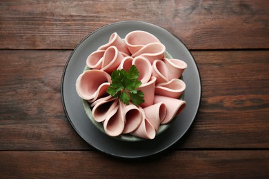 Photo of Slices of delicious boiled sausage with parsley on wooden table, top view