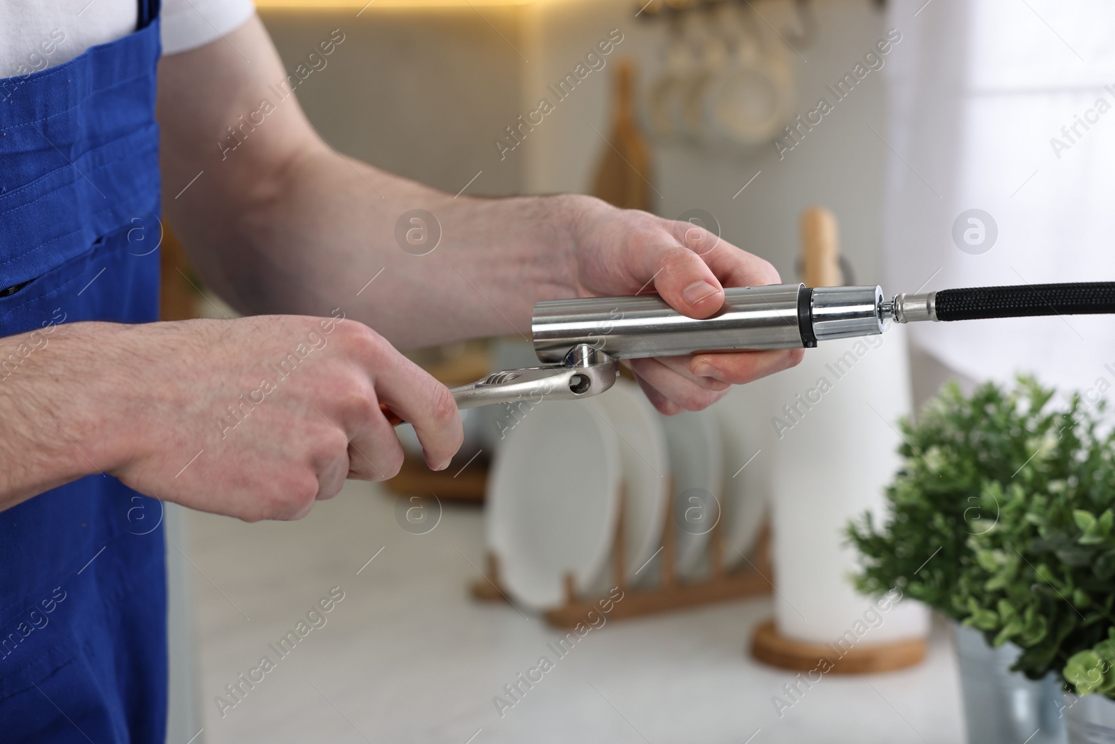 Photo of Plumber repairing faucet with spanner in kitchen, closeup