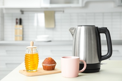 Photo of Modern electric kettle, cup and honey on wooden table in kitchen