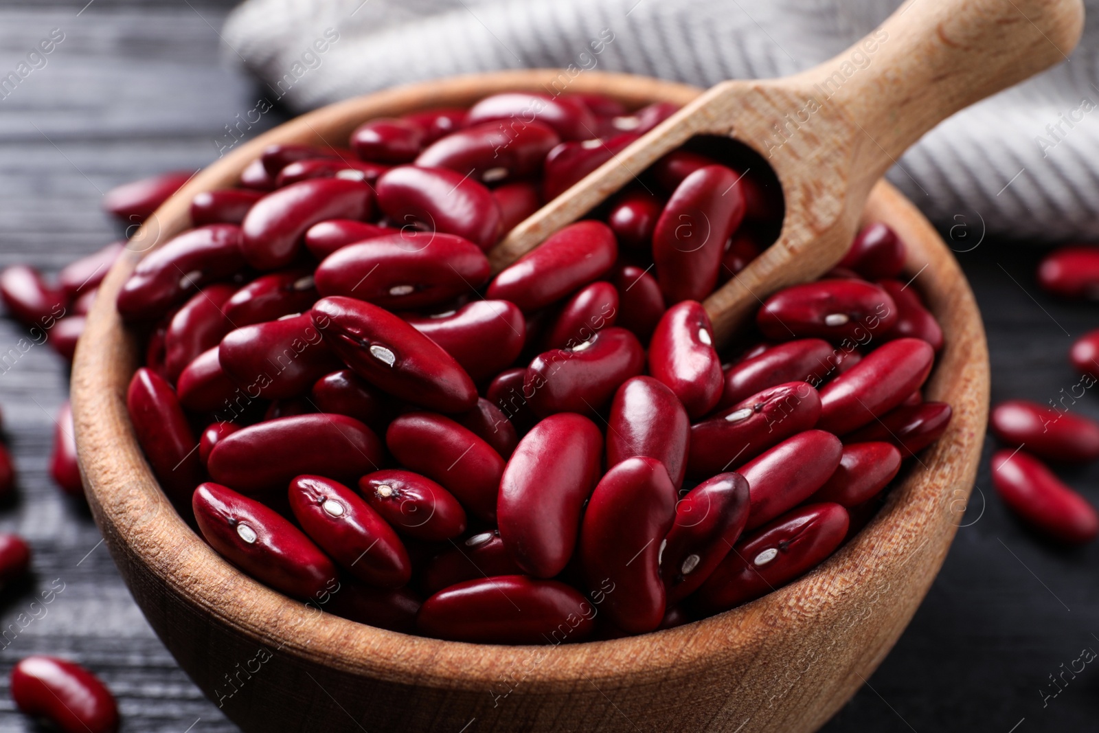 Photo of Raw red kidney beans in wooden bowl and scoop on table, closeup