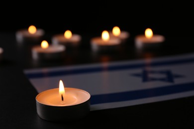 Photo of Burning candle and flag of Israel on black table. Holocaust memory day