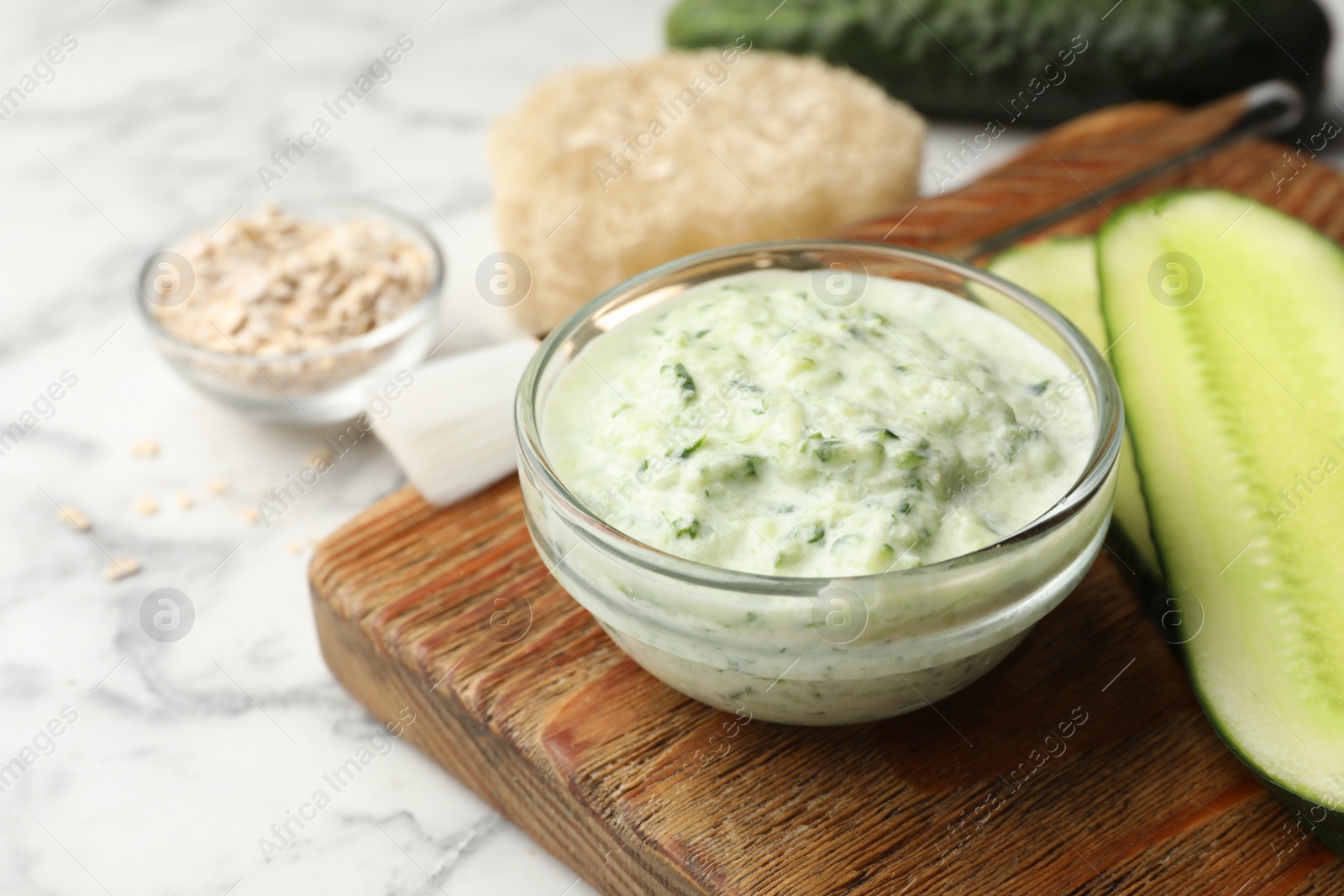 Photo of Handmade cucumber face mask in glass bowl and ingredients on marble table