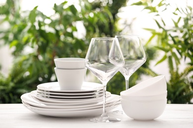 Photo of Set of clean dishware and wineglasses on white table against blurred background