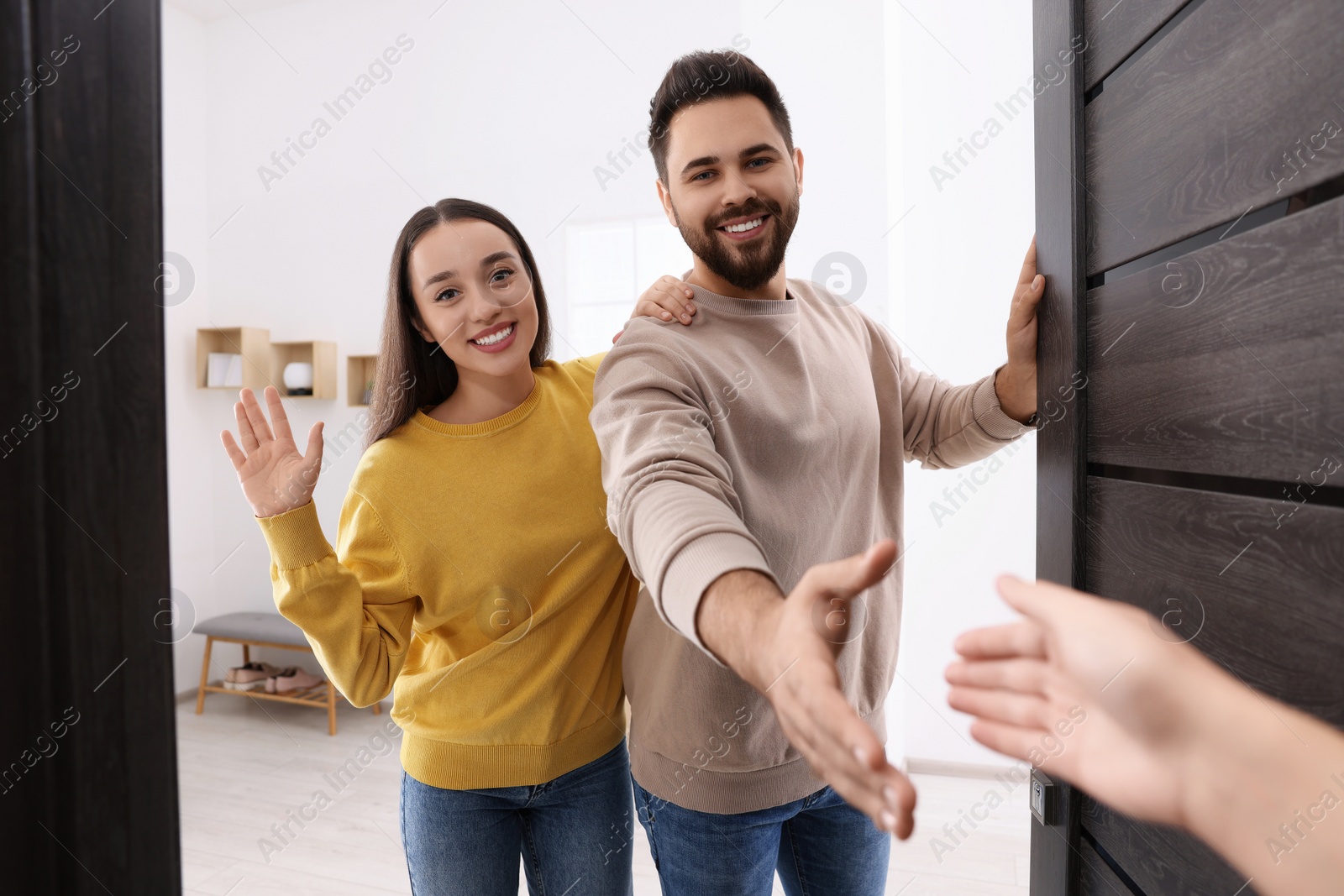 Photo of Happy couple welcoming their guest near door. Invitation to come indoors