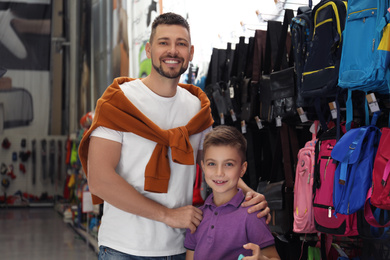 Photo of Little school boy with father choosing backpack in supermarket