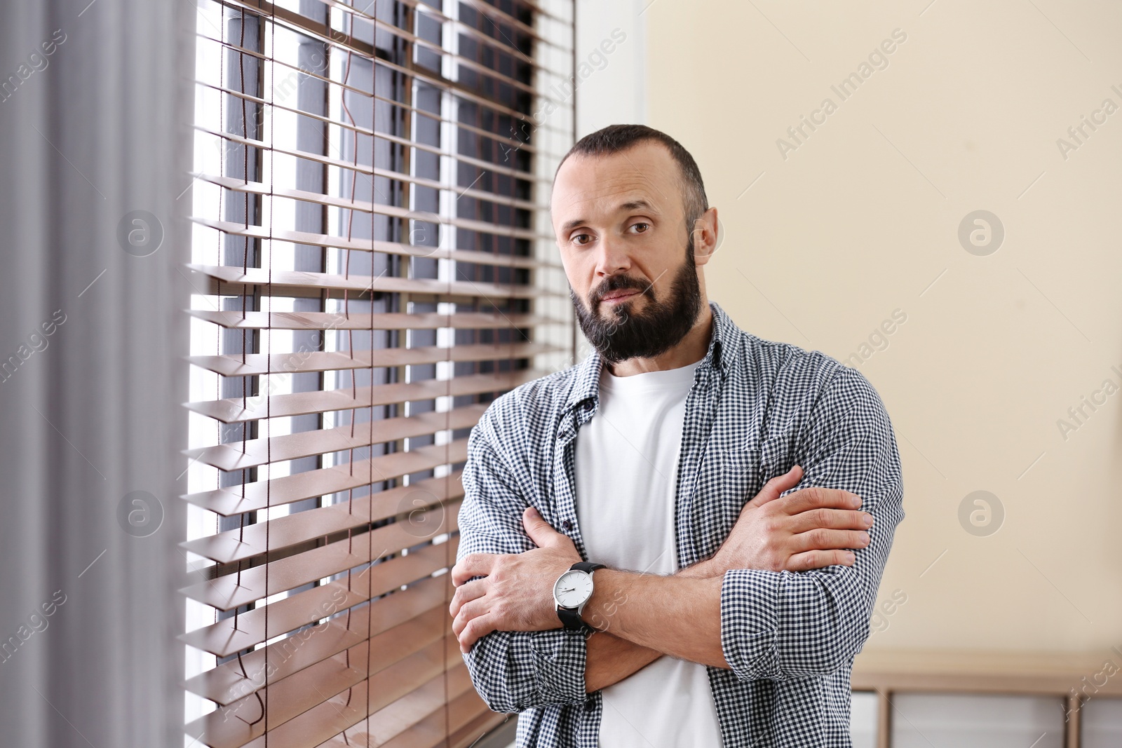 Photo of Portrait of handsome mature man near window with blinds indoors