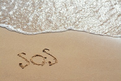 Message SOS drawn on sandy beach near sea
