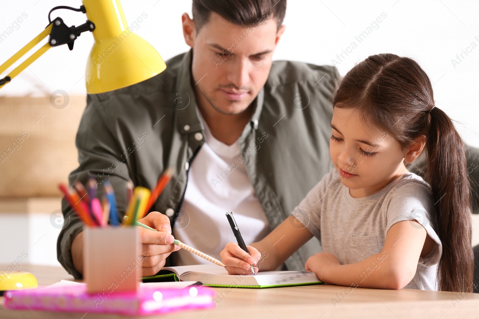 Photo of Man helping his daughter with homework at table indoors