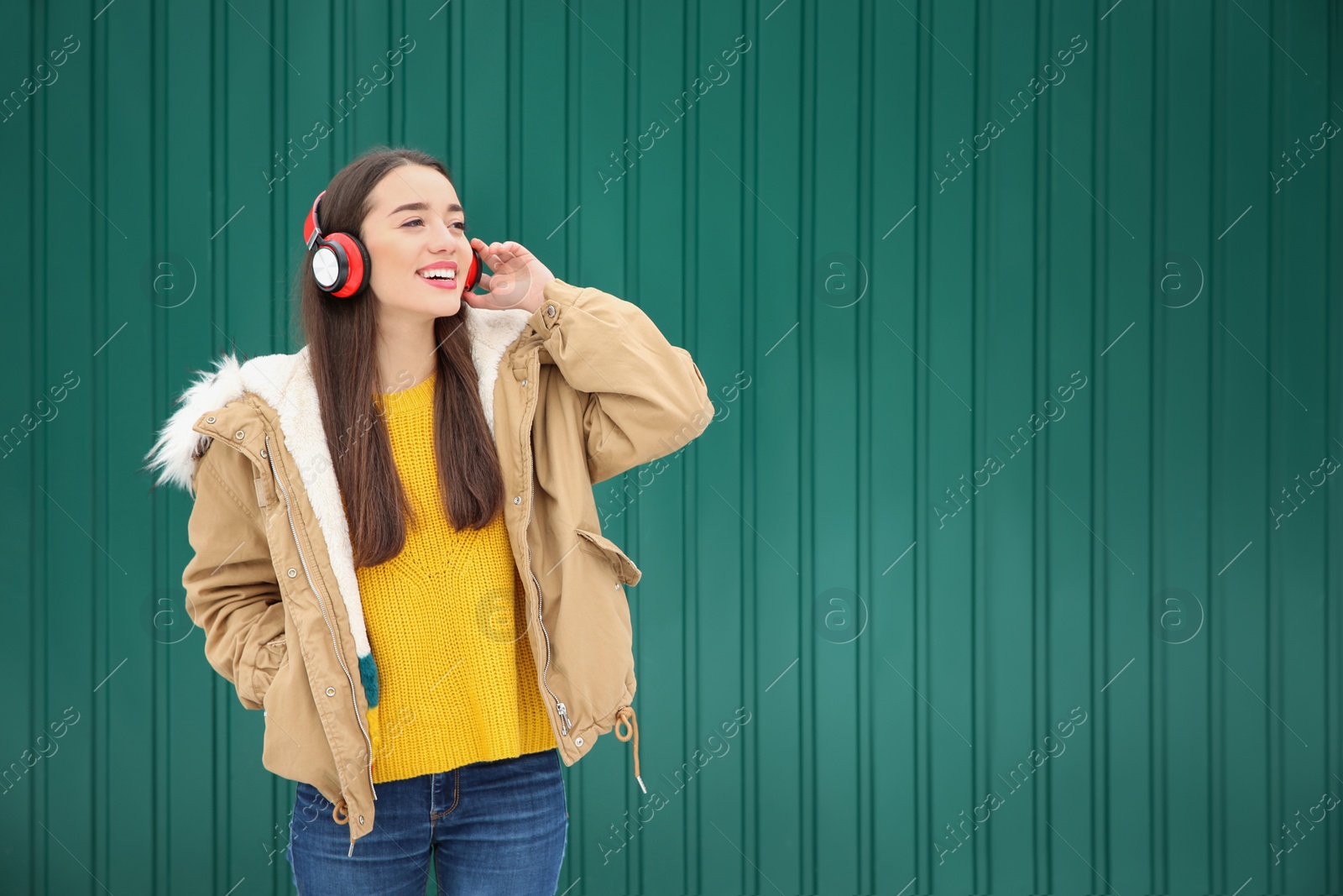 Photo of Beautiful young woman listening to music with headphones against color wall. Space for text