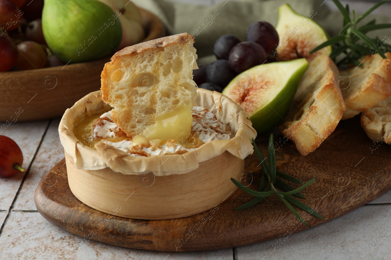 Photo of Tasty baked brie cheese, bread and other products on light tiled table