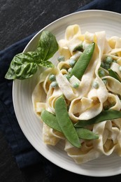 Photo of Delicious pasta with green peas and creamy sauce on black table, top view