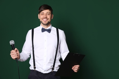 Handsome man in formal clothes posing with microphone and clipboard on color background. Space for text