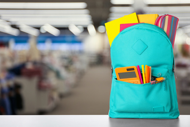 Bright backpack with school stationery on table in shopping mall. Space for text