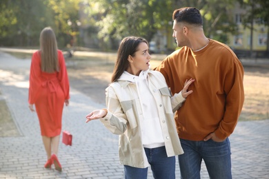 Disloyal man looking at another woman while walking with his girlfriend in park