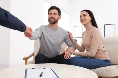 Photo of Real estate agent shaking hands with client at table in office, closeup
