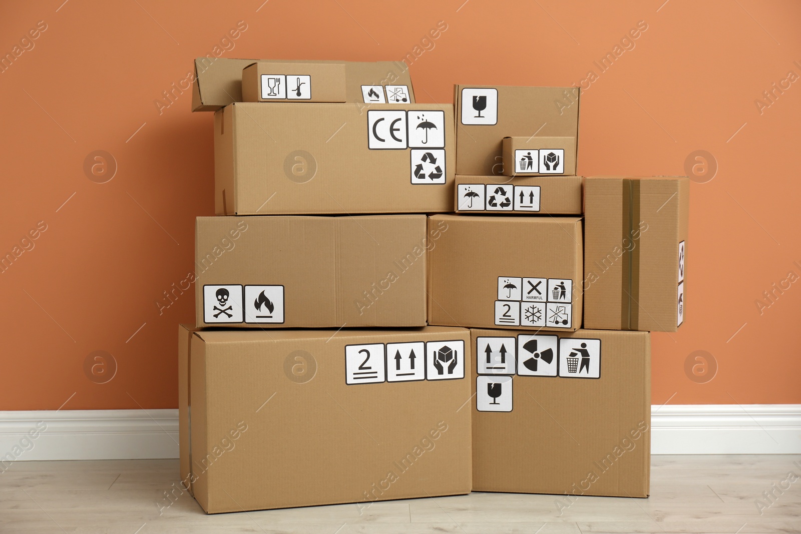 Photo of Cardboard boxes with different packaging symbols on floor near orange wall. Parcel delivery