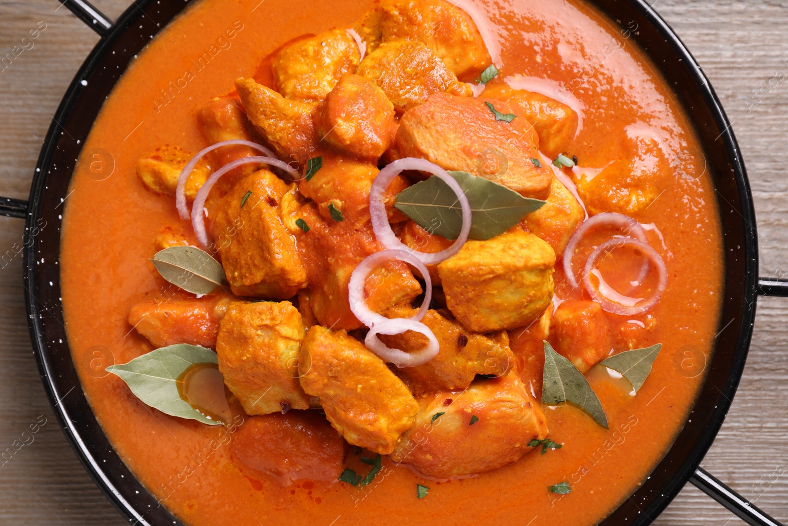 Photo of Delicious chicken curry in pan on wooden table, top view