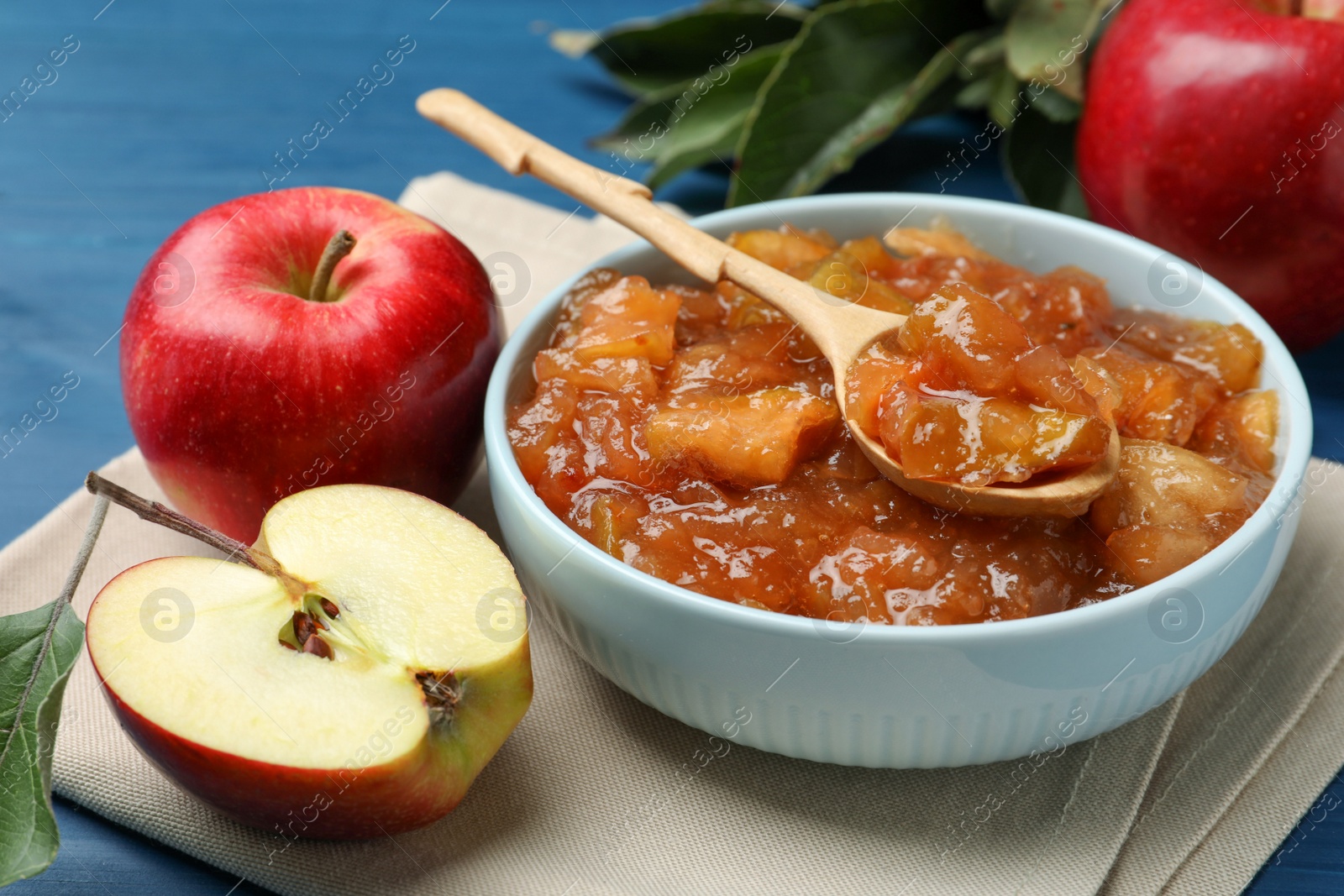 Photo of Tasty apple jam in bowl and fresh fruits on blue table