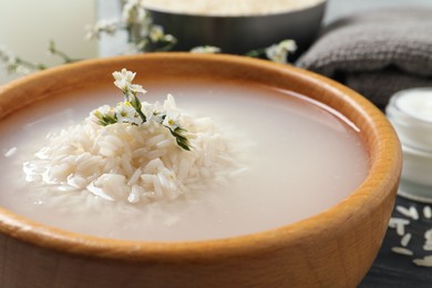 Photo of Wooden bowl with soaked rice in water on table, closeup