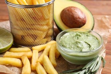 Photo of Parchment with french fries, guacamole dip, lime and avocado served on wooden table, closeup